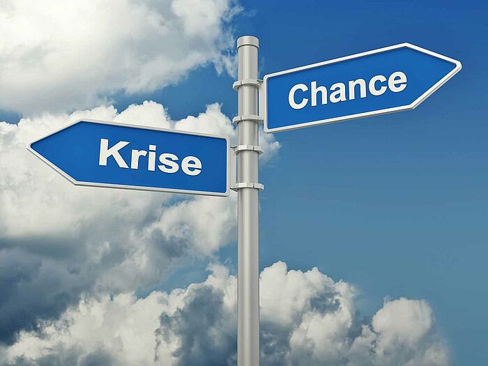 Zwei Hinweisschilder mit den Titeln "Krise" und "Chance" zeigen in unterschiedliche Richtung