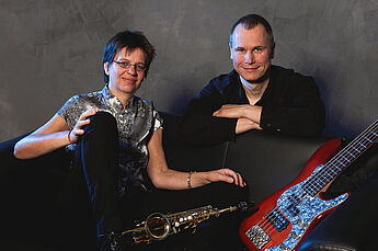 Die Musiker:innen sitzen mit ihren Instrumenten auf einem Sofa