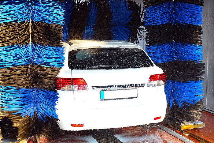 Ein weißes Fahrzeug, zu sehen von hinten, in der Waschstraße, zwischen zwei blau-schwarz gestreiften Bürsten